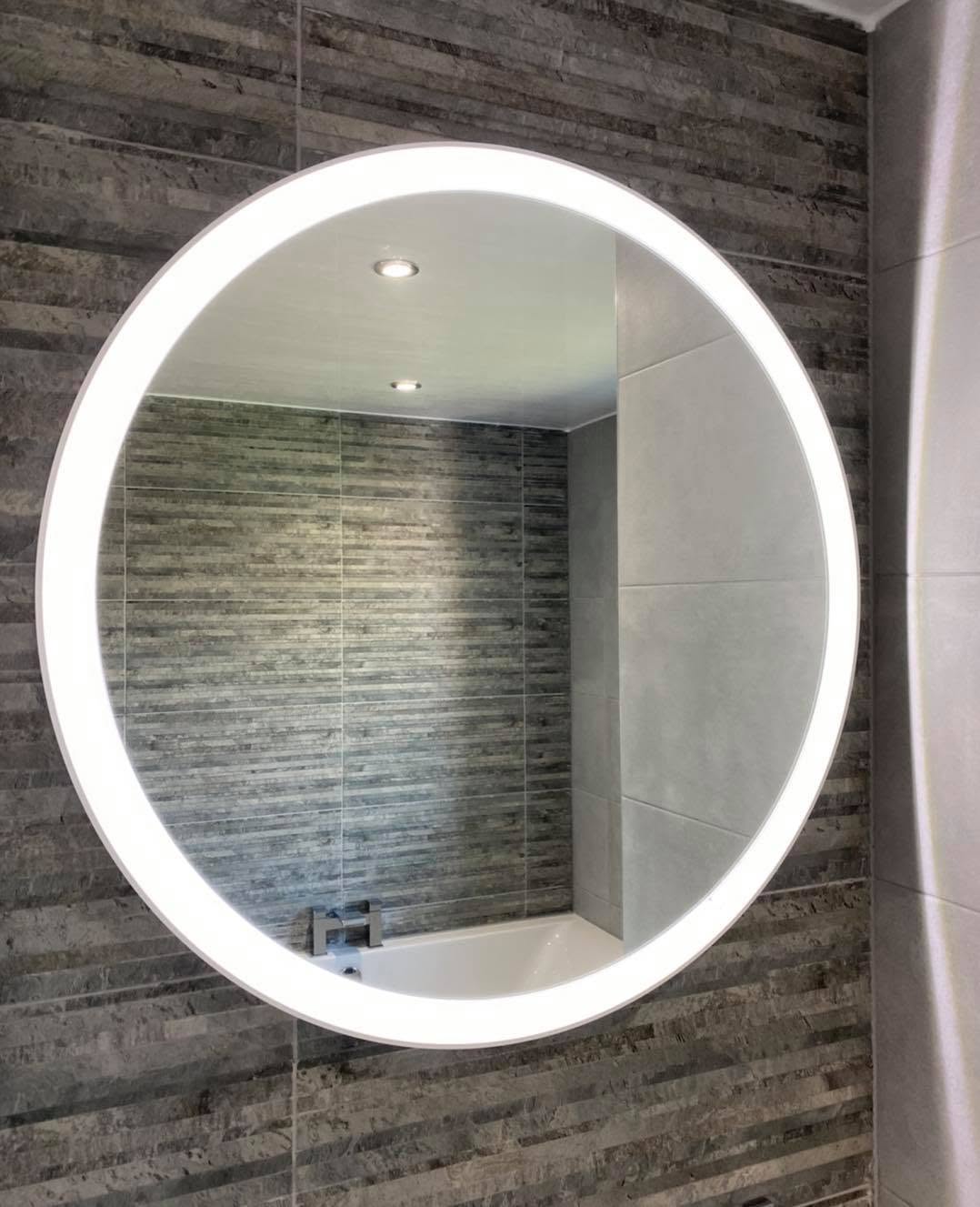 Round backlit LED bathroom mirror against stone-effect tiling